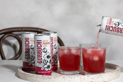 A person pouring a refreshing drink into a glass from a can of Gurbuchi, showcasing the vibrant beverage and the can's design.