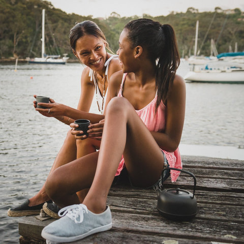 Two women on a jetty smiling at each other drinking Guradji tea