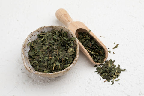 A bowl filled with Guradji Tisane tea leaves accompanied by a wooden spoon, showcasing natural ingredients for tea preparation.