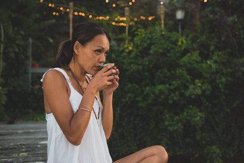  A woman relaxes on a wooden jetty, sipping LORE Australia Guradji tea, surrounded by a peaceful natural environment.